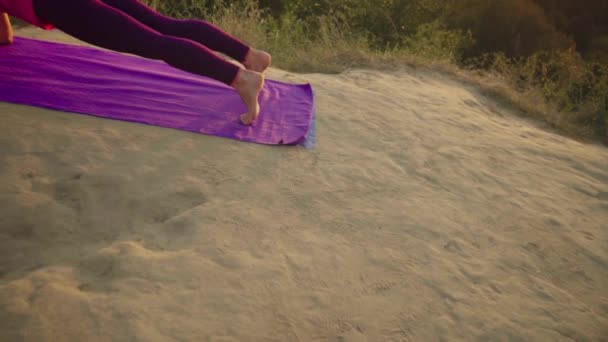 Молодая женщина практикует йогу на горе на фоне большого города. Здоровая женщина занимается спортом на закате. Спортсмен в розовой рубашке и фиолетовых леггинсах разминается на рассвете. . — стоковое видео