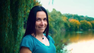 Siyah saçlı genç gülümseyen kadın portresi. Gamzeleri olan bir kız. Kadın yakın göl gün batımında.