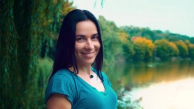 Siyah saçlı genç gülümseyen kadın portresi. Gamzeleri olan bir kız. Kadın yakın göl gün batımında.