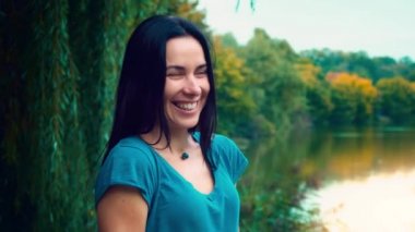 Siyah saçlı genç gülümseyen kadın portresi. Gamzeleri olan bir kız. Kadın yakın göl gün batımında.