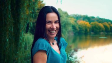 Siyah saçlı genç gülümseyen kadın portresi. Gamzeleri olan bir kız. Kadın yakın göl gün batımında.