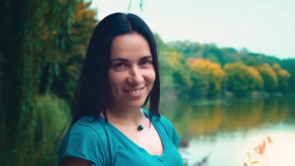 Porträtt av en ung leende kvinna med svart hår. En flicka med gropar. Kvinna nära sjön vid solnedgången på dagen. — Stockvideo