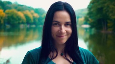 Siyah saçlı genç gülümseyen kadın portresi. Gamzeleri olan bir kız. Kadın yakın göl gün batımında.