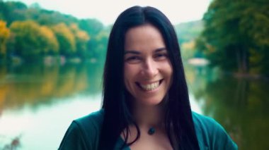 Siyah saçlı genç gülümseyen kadın portresi. Gamzeleri olan bir kız. Kadın yakın göl gün batımında.