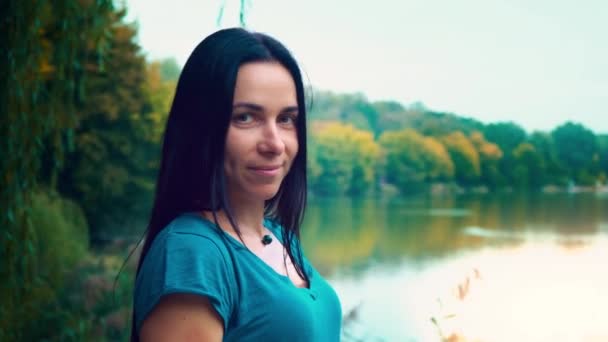 Retrato de uma jovem mulher sorridente com cabelo preto. Uma rapariga com covinhas. Mulher perto do lago ao pôr-do-sol do dia . — Vídeo de Stock