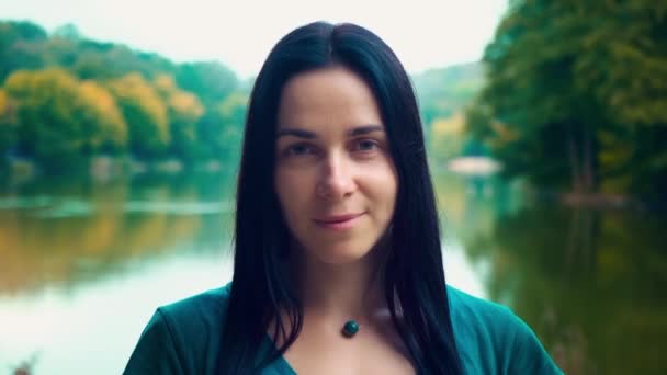 Retrato de uma jovem mulher sorridente com cabelo preto. Uma rapariga com covinhas. Mulher perto do lago ao pôr-do-sol do dia . — Vídeo de Stock