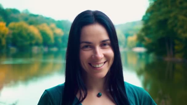 Retrato de uma jovem mulher sorridente com cabelo preto. Uma rapariga com covinhas. Mulher perto do lago ao pôr-do-sol do dia . — Vídeo de Stock