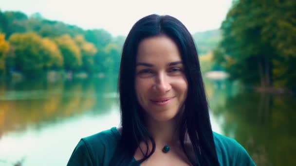 Portréja egy fiatal, mosolygós nő fekete hajjal. A lány gödröcskék. Nő a tónál, napnyugtakor a nap. — Stock videók