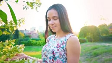 Gülümseyen bir esmer yeşil park karşı çukurlu yanakları portresi. Güzel genç kadın parkta duruyor ve kameraya benziyor. Çiçek baskı ile yaz elbiseli güzel kız