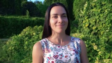 Yeşil park karşı çukurlu yanakları güzel bir genç kadın portresi. Yavaş yavaş esmer gülümseyen bahçede yeşil çalılar boyunca yol gösterir. Çiçek baskı ile yaz elbiseli güzel kız