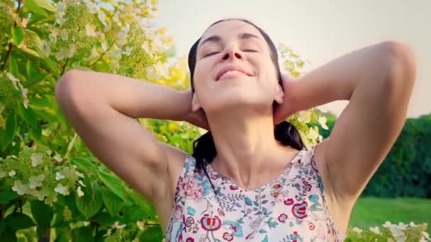 Portrait d'une brune souriante aux joues ondulées contre un parc verdoyant. La fille regarde la caméra et joue avec ses cheveux. Belle jeune femme se tient dans le parc et regarde la caméra — Video