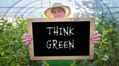 Bir kadın çiftçi organik sebze ve meyve almaya davet ediyor. Elinde tabela olan gülümseyen kadın sağlıklı yemek ister. Vejetaryenlik, vejetaryenlik. Sera, aile sebze yetiştirme işi.