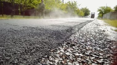 Yağmurda asfalt seriyorum. Yeni bir yol inşaatı. Patinaj seviyesi asfaltı sıkıştırıyor. İnşaat makineleri küçük bir kasabada, köyde yol yapıyor. Sanayileştirme