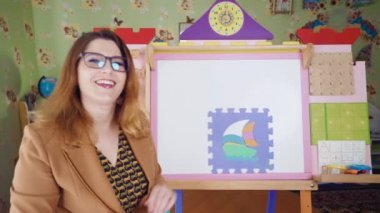 Çocuklar için uzaktan öğrenme. Yeni Kelimeler Öğreniyorum. Bir anaokulu öğretmeni çevrimiçi bir ders veriyor. E-öğrenme. Evde eğitim. Genç öğretmen bulmaca parçalarının teknesini topluyor..