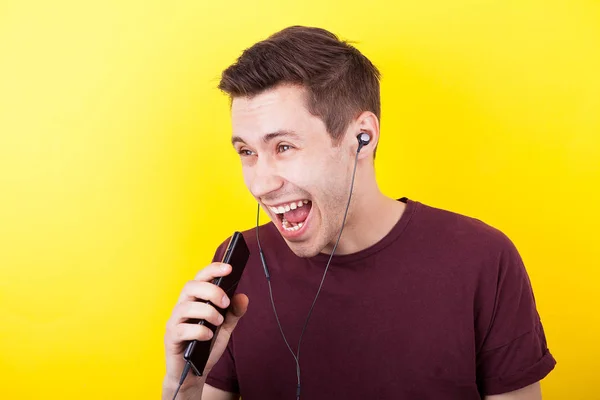 Hombre feliz cantando en su teléfono como un micrófono y con auriculares en los oídos —  Fotos de Stock