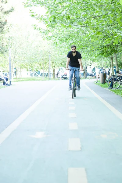 Jovem barbudo montando uma bicicleta no parque — Fotografia de Stock