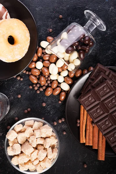 Vista superior de cacahuetes en chocolate, derramados en la pizarra oscura, junto a tabletas de chocolate, donas, azúcar morena y granos de café —  Fotos de Stock