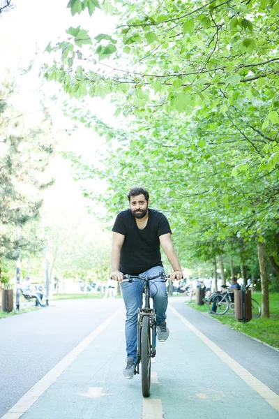 Jovem barbudo montando uma bicicleta no parque — Fotografia de Stock