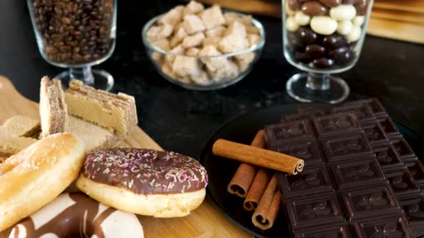 Donuts e waffles ao lado de chocolate escuro e paus de canela — Vídeo de Stock