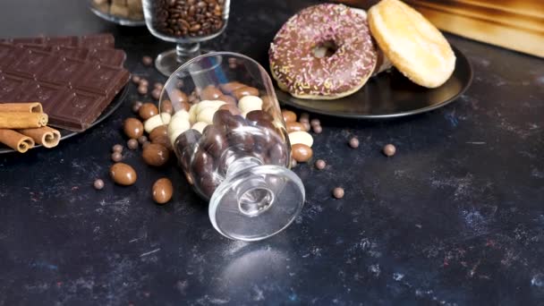他のキャンディーの横に木製の背景にあるチョコレートにピーナッツを転覆させたガラス — ストック動画