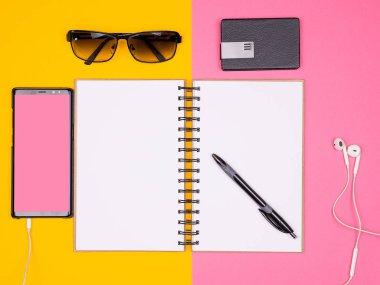 Açık Kağıt defter bir kalem, güneş gözlüğü ve iki renkli arka plan üzerinde kulaklık ile smartphone yanında