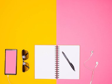 Açık Kağıt defter bir kalem, güneş gözlüğü ve iki renkli arka plan üzerinde kulaklık ile smartphone yanında