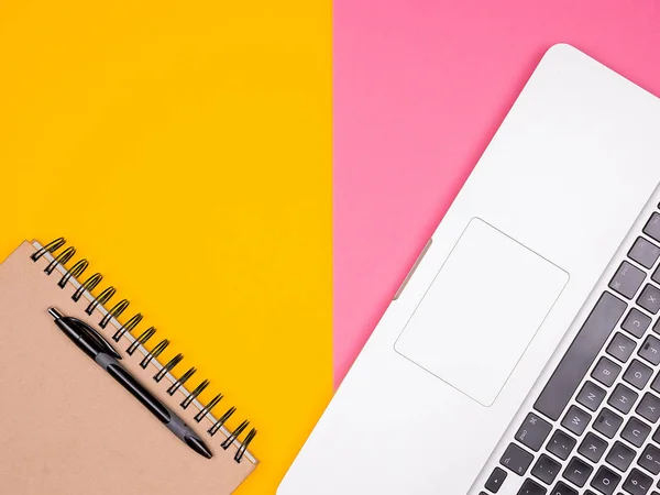 Caderno de papel com uma caneta ao lado de um laptop em dois fundos coloridos — Fotografia de Stock