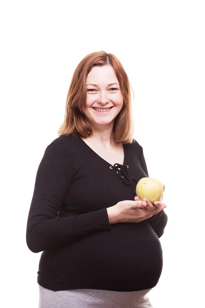 Беременная женщина улыбается в камеру, держа в руках яблоко — стоковое фото