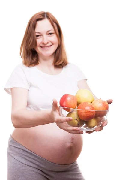 Mulher grávida sorrindo para a câmera e segurando uma tigela de vidro com frutas em suas mãos — Fotografia de Stock