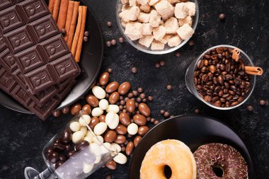 Tablet çikolatalar, çörek, kahverengi şeker ve çikolata fıstık ile diğer cam yanında kahve çekirdekleri ile cam