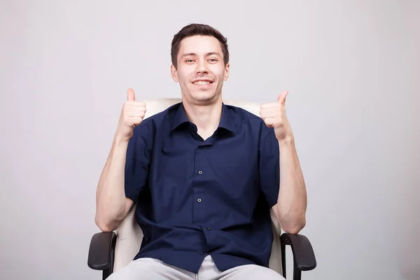 Jungunternehmer in lässigem blauem Hemd zeigt Daumen in die Kamera, während er im Bürostuhl sitzt — Stockfoto