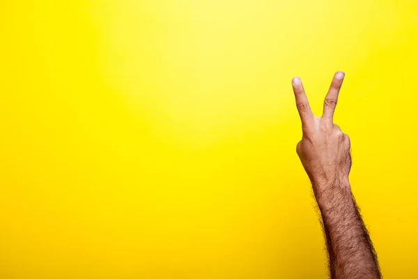 Mâna arată un semn de victorie pe un fundal galben — Fotografie, imagine de stoc