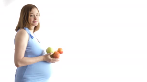 Beautiful pregnant woman enters the frame with a bowl of apples in hands — Stock Video