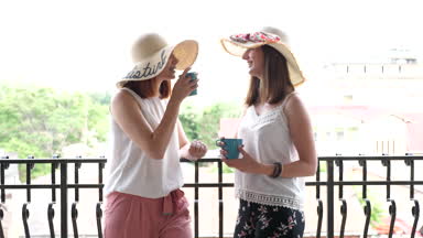 Balkonda kahve içme ve konuşmaya büyük yaz şapka iki güzel genç bayanlar