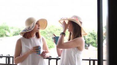 Çekim iki güzel ve muhteşem kadın üzerinde balkon içme kahve büyük şapkalar ile ortaya