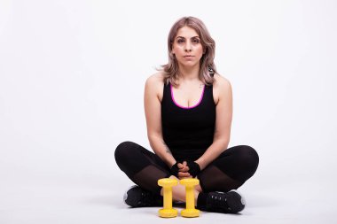 Onun yanında iki küçük dumbbells ile uzanarak spor giyim kadın. Studio fotoğraf. Gri arka planı