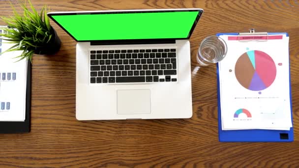 Laptop com tela verde e duas pranchetas em uma mesa — Vídeo de Stock