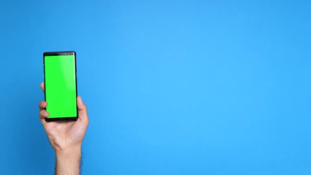 Hombre levantando la mano y sostiene un teléfono inteligente con pantalla azul — Vídeos de Stock