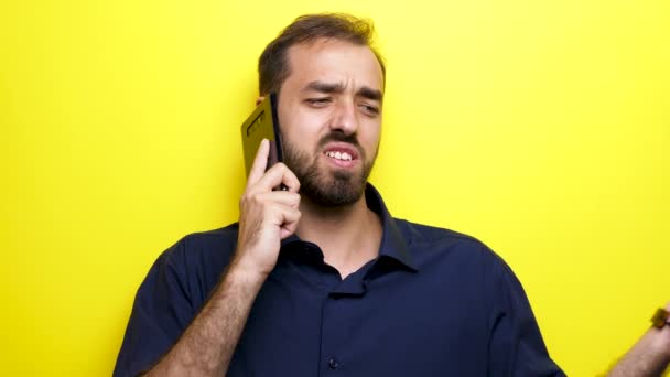 Мужчина в обычной синей рубашке разговаривает по телефону на жёлтом фоне — стоковое видео