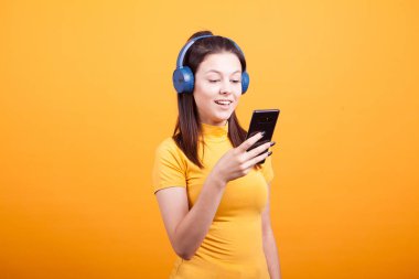 Sevimli genç kadın manifatura Studio sarı zemin üzerine müzik dinleme sırasında telefonunda