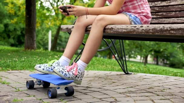 Fechar os pés menina em um skate sentado em um banco — Vídeo de Stock