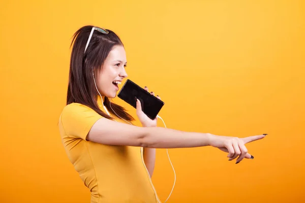 Jeune femme mignonne chantant sur son téléphone et pointant — Photo