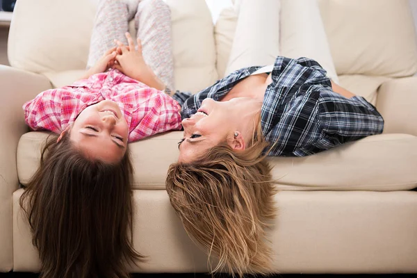 Beautiful mother with her cute daughter lying on the couch with their head upside down