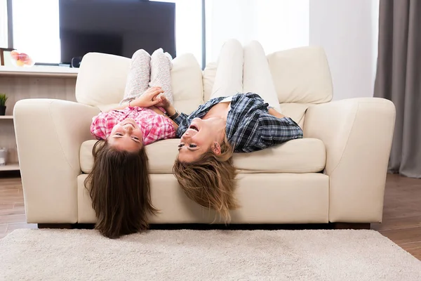 Beautiful mother with her cute daughter lying on the couch with their head upside down