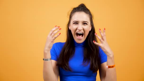 Τονίζει και συναισθηματική γυναίκα ουρλιάζοντας στο studio πάνω από έντονο πορτοκαλί φόντο — Αρχείο Βίντεο