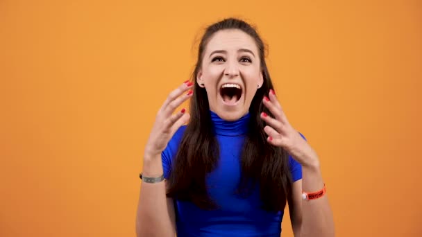 Napětí a emocionální žena nosí modré tričko křik ve studiu nad zářivé oranžové pozadí — Stock video