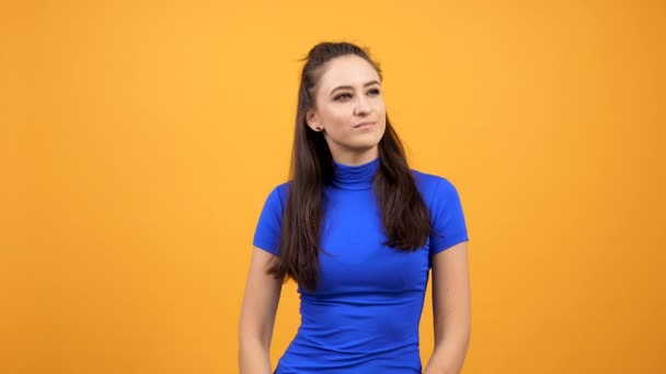 Hermosa mujer en camiseta azul aburrida sobre fondo naranja vívido en el estudio — Vídeo de stock