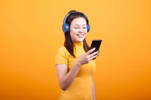 Söt ung kvinna textning på sin telefon när du lyssnar musik — Stockfoto