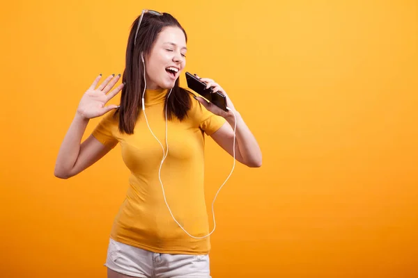 Bonito jovem mulher cantando enquanto ouve música em seu telefone — Fotografia de Stock