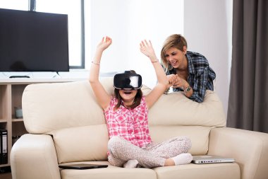 Anne bir sanal gerçeklik kulaklık giyen kızı yanında oturan oturma odasında